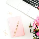 laptop, pink flowers and pink notebook on white desk