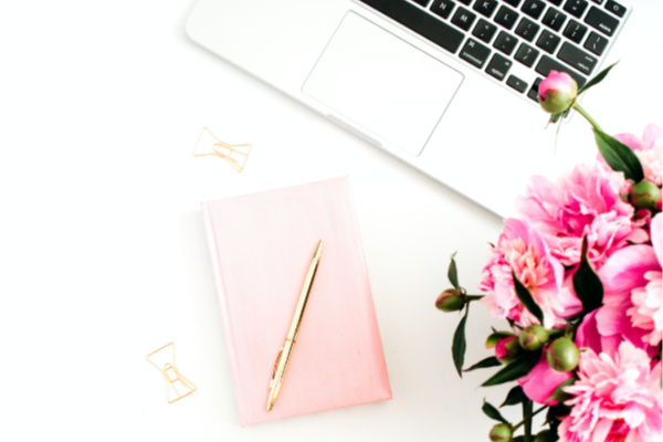 laptop, pink flowers and pink notebook on white desk