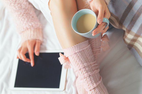 Woman using tablet at cozy home atmosphere on the bed with cup of coffee