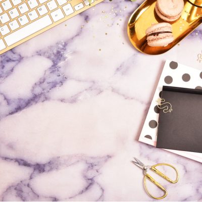 gold computer keyboard, polka dot notebook and gold accessories on purple marble background