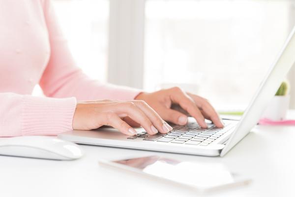 shot of woman's chest and arms wearing a pink top while typing on a laptop